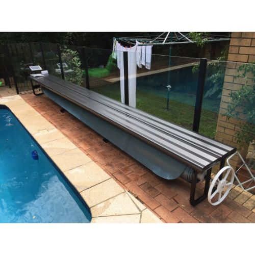 Daisy Under Bench Pool Cover Roller (Powered) in Charcoal Shimmer beside a modern swimming pool